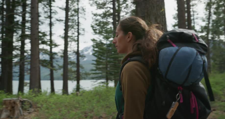 Woman wearing a backpack walking on a trail through the pine tree forest near a lake
