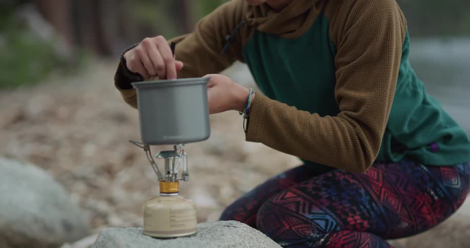 Woman cooking a meal in a small por over a portable stove while camping
