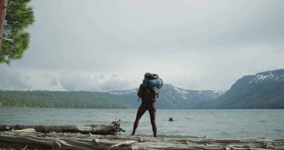 A woman out hiking walks towards the shore and looks out at the water
