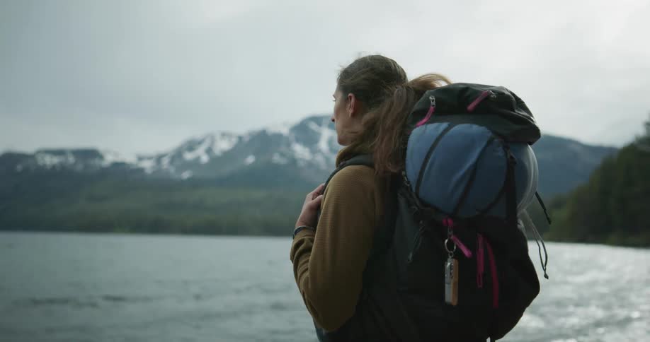 A backpacker stands in front of a lake and takes in the view of the water and mountains