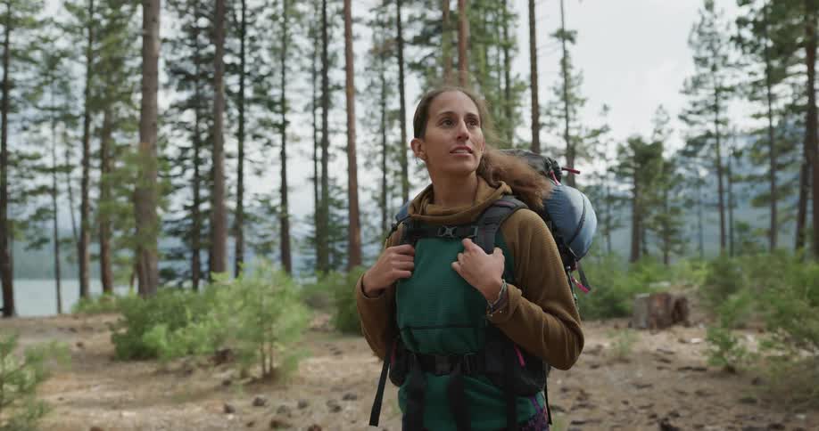 A backpacker looks up at the tall trees as she stands on a trail in the woods