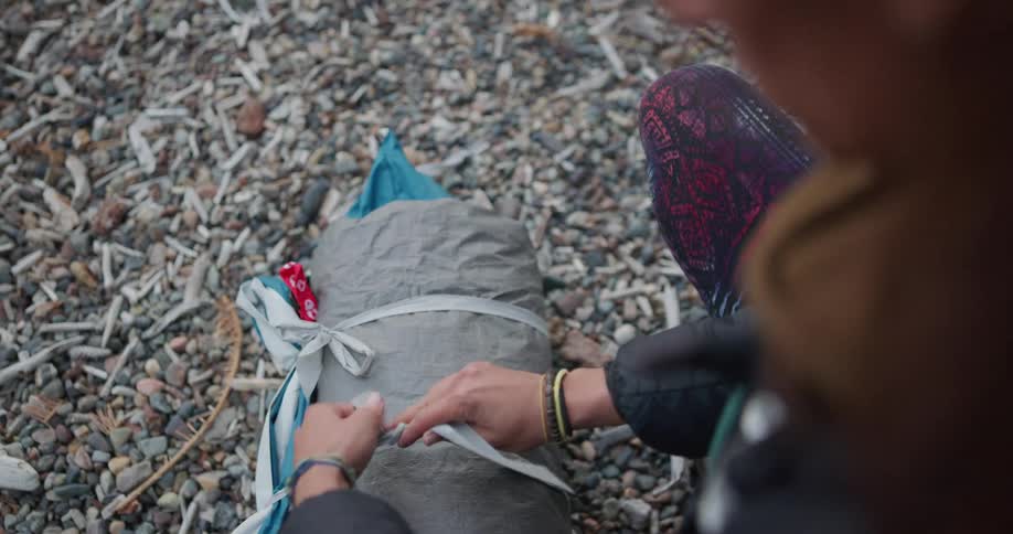 A woman squats down while tying up the strings to secure her camping sleeping roll