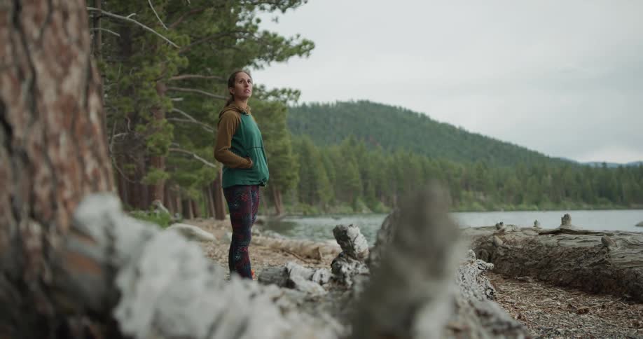 A woman stands on the shore and looks out at the water