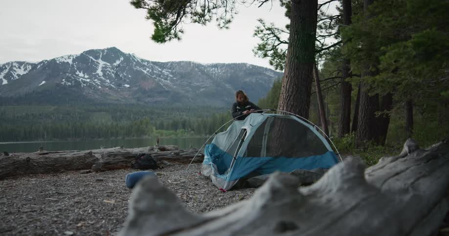 Woman dismantling a tent in the wilderness near a lake