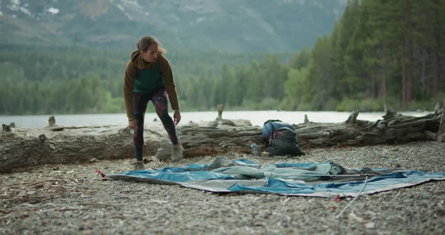 A woman setting up a tent next to a lake in a forest at daytime
