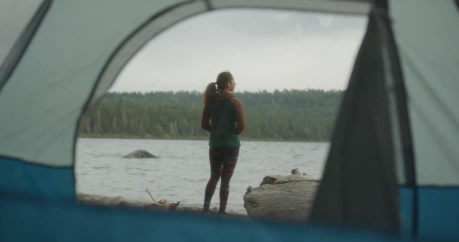 Interior view from tent of a woman standing at lakes shoreline enjoying the scenery