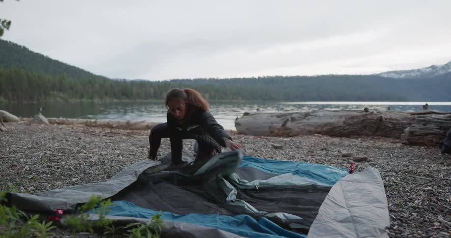 A woman folds up a tent on the shore
