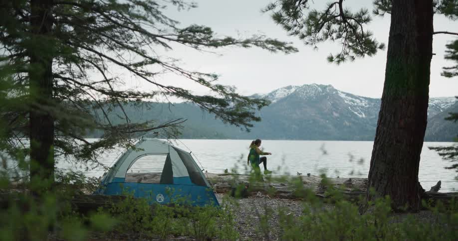 Woman camping near a lake in the pine tree forest on the mountains
