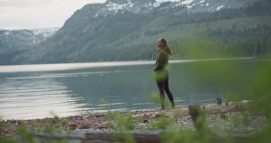 Young woman standing on the shore of a lake near the pine tree forest in the mountains