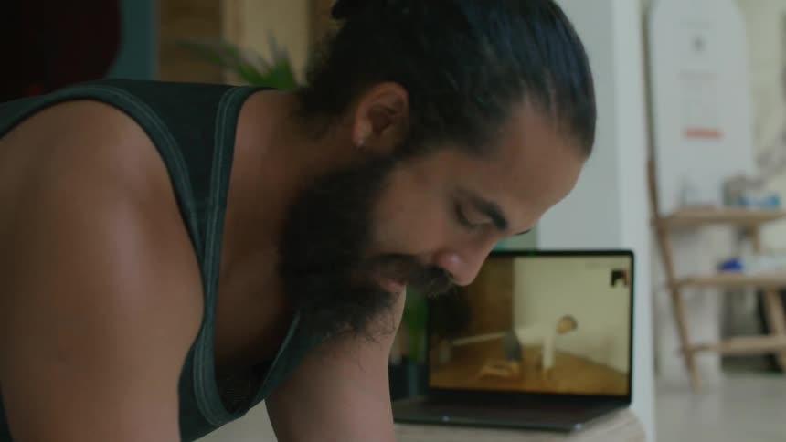 A man stretching while watching an instructional video on laptop