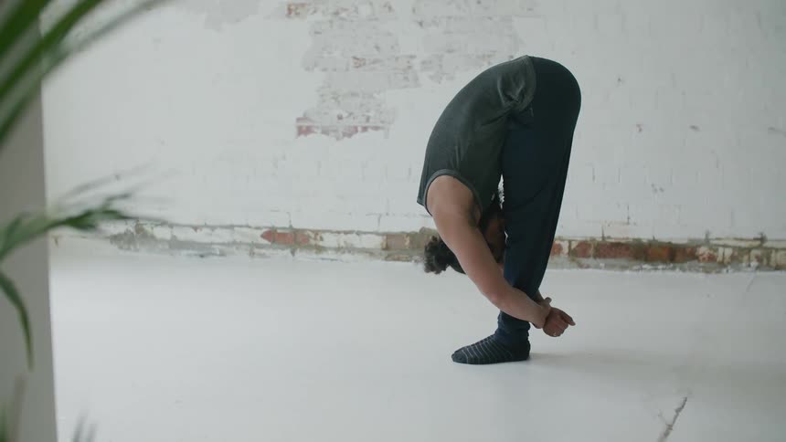 Bearded man wearing sports clothes doing yoga stretches up and down standing on a room