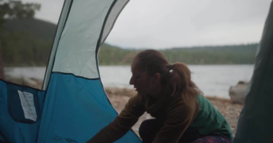 A woman putting a sleeping bag inside a tent on a lakeshore
