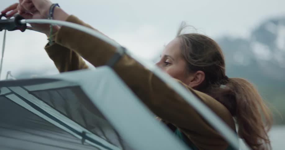 A woman is putting a tent up outdoors