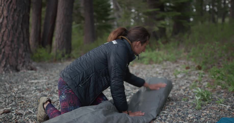 A woman in a forest folds up a tent