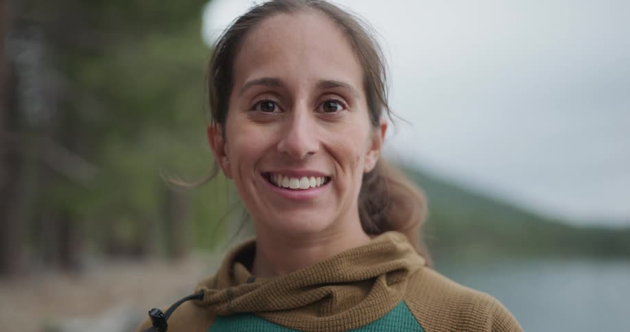 Woman camping in the woods near a lake in the mountains looking at the camera smiling