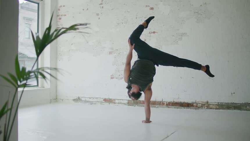 A man puts his hands down on the floor and does a hand stand along with other poses