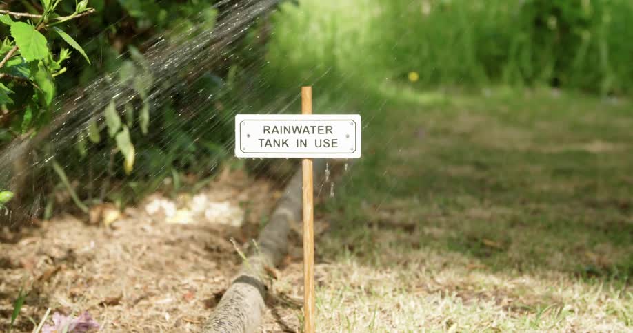 Sign of rainwater tank in use while a person waters plants in a garden