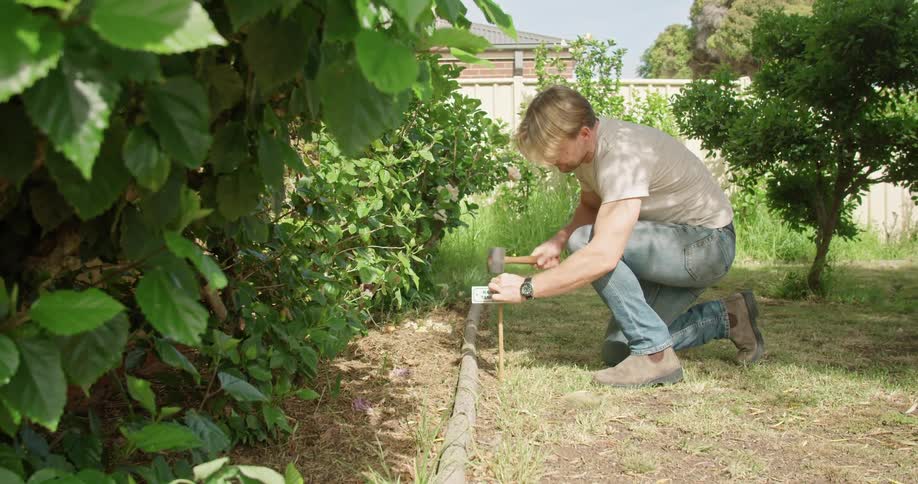 A man in his back yard hammers a sign in to his lawn