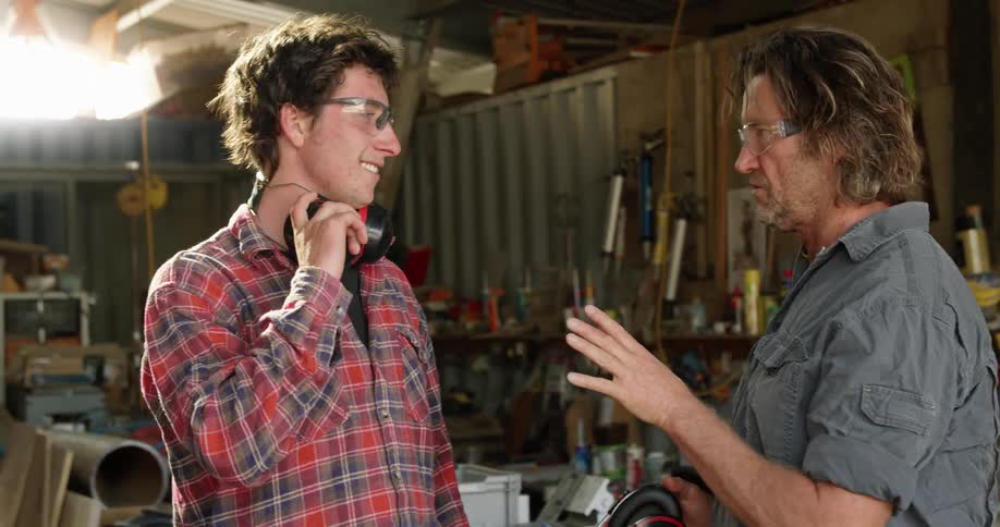 Father teaching son how to use power tools to cut lumber in the workshop