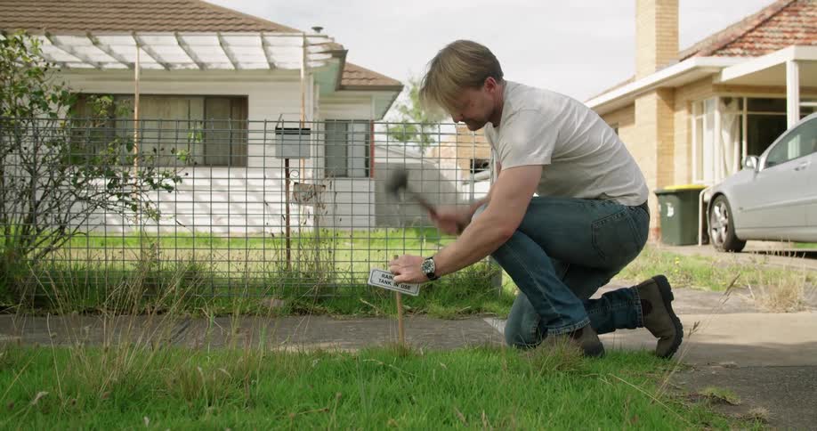 Man hammering down a small sign on the lawn in front of his home