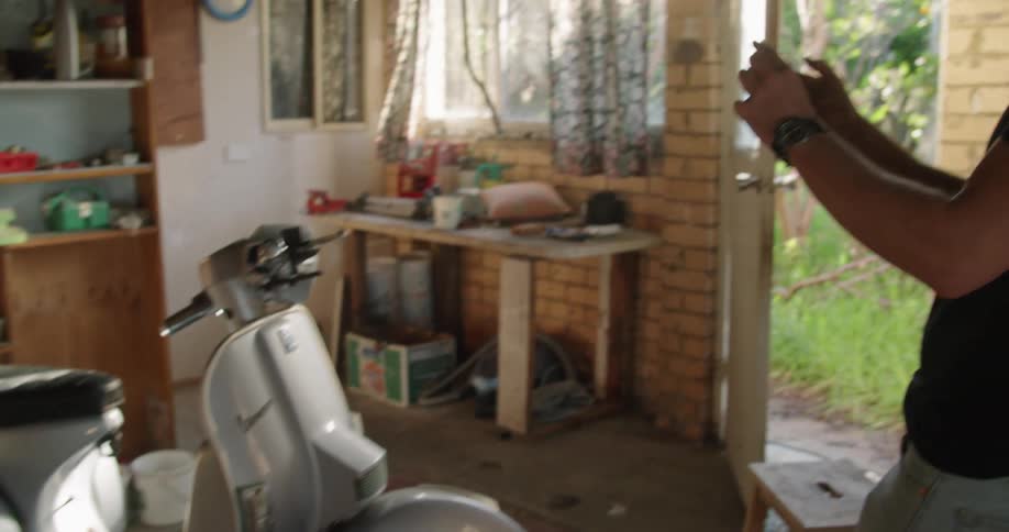 A man takes a picture of a silver moped with a smart phone camera in a garage at home at daytime