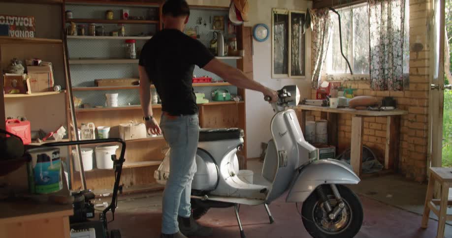 A man starting a vespa motorcycle on the garage at home