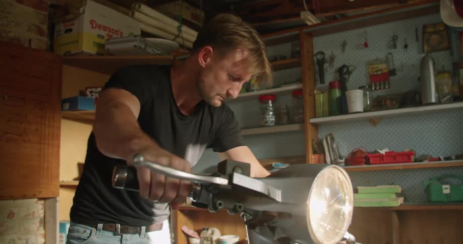 A man starting a vespa motorcycle on the garage at home