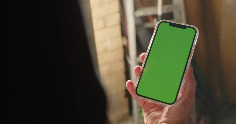 A person in a room holding a smart phone with a wall and a ladder in the background