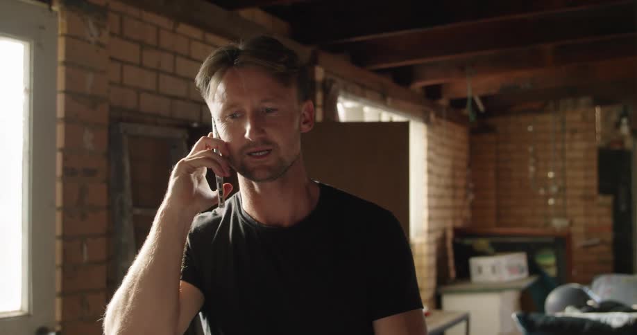 A man talks on the phone standing inside a home then puts the phone in his pocket when finished