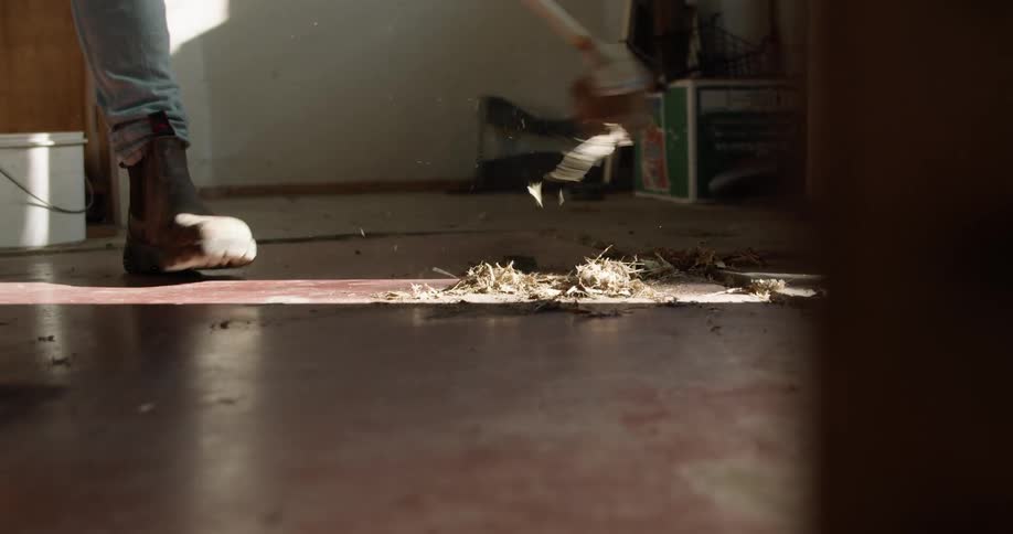 A person sweeping debris into a pile on a floor indoors with a broom