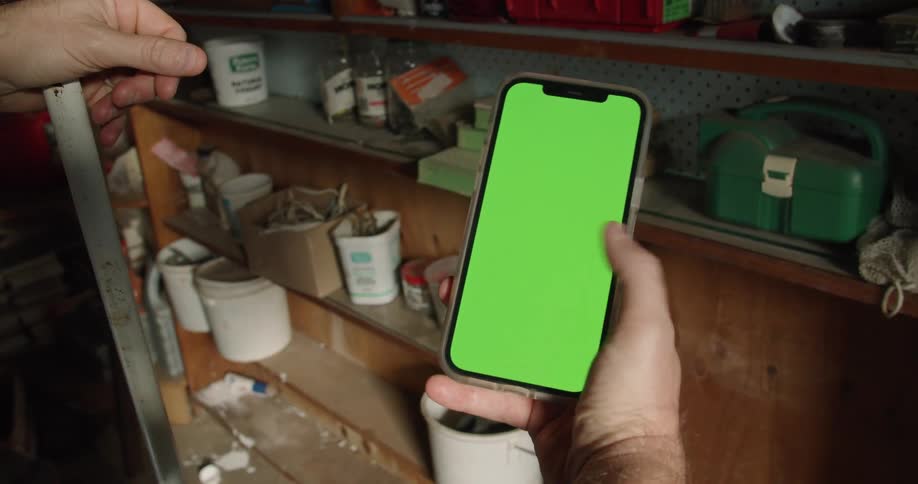 A man swipes through his smartphone while standing in front of shelves filled with cleaning equipment