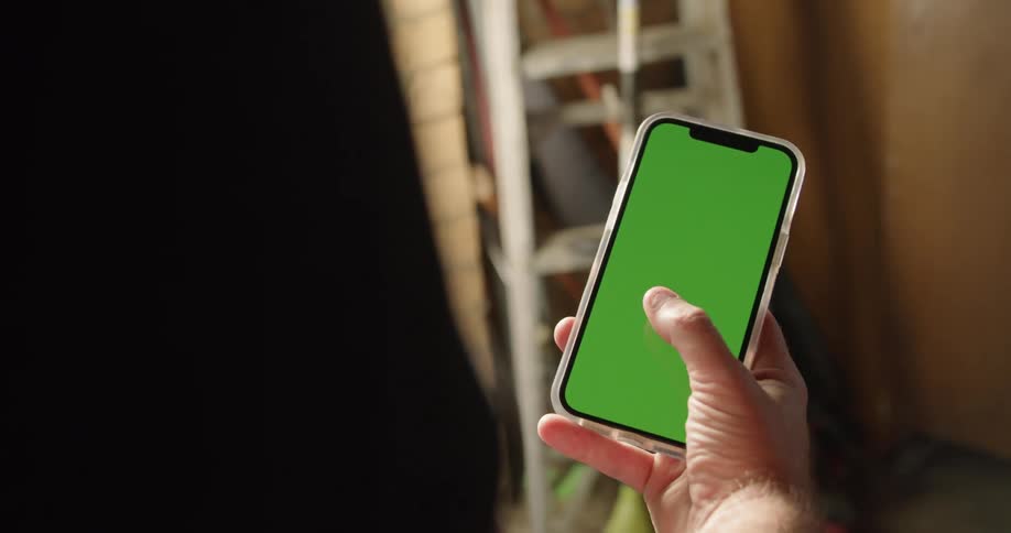 A person in a room using a smart phone with a wall and ladder in the background