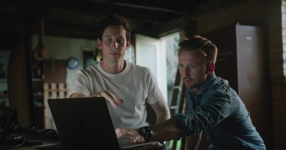 Two men are sitting by a laptop indoors