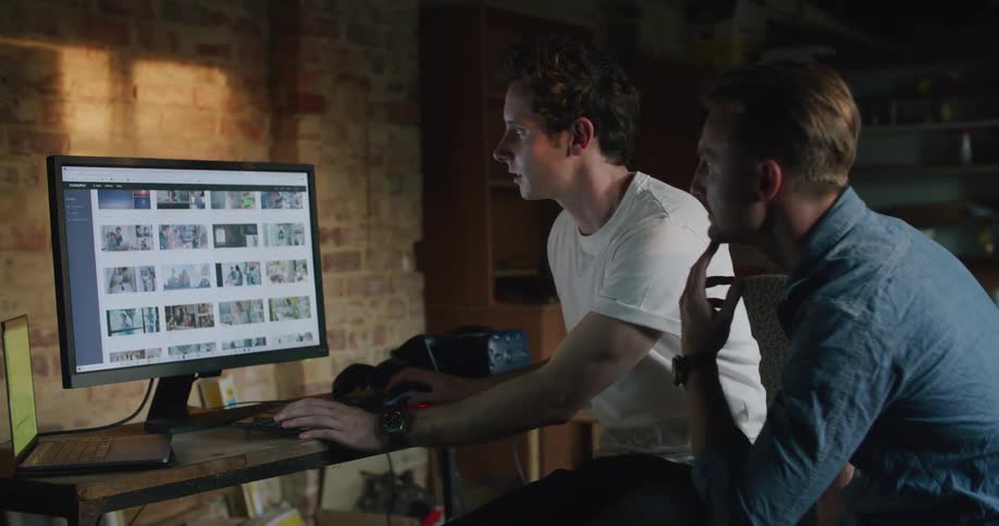 A man points to and shows images on a computer screen as he discusses them with another