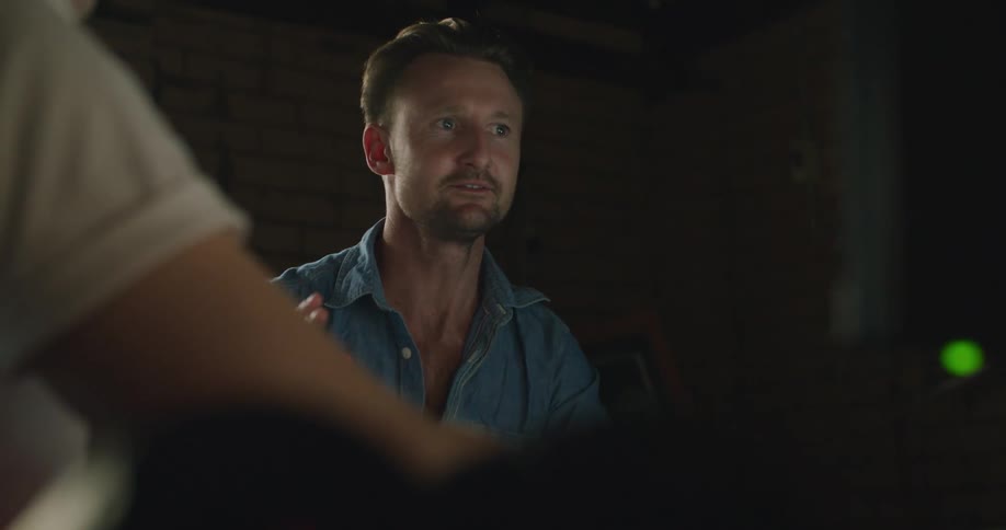 Two men in a room sitting and talking with a monitor in the foreground and a wall and window in the background