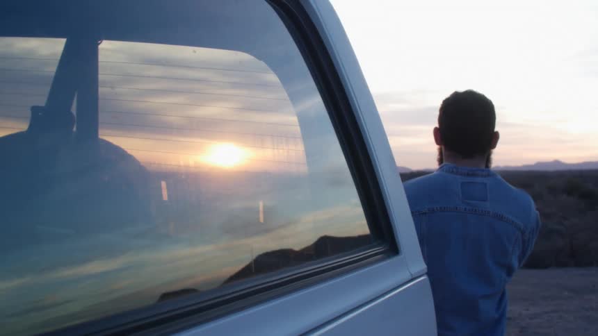 A man is standing by his car outdoors at dusk