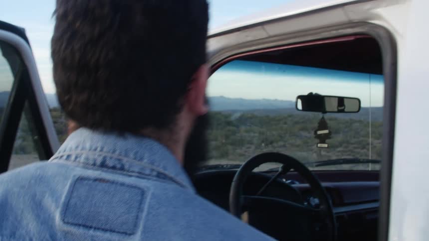 Bearded man boards a pickup truck parked on a rural road at sunset