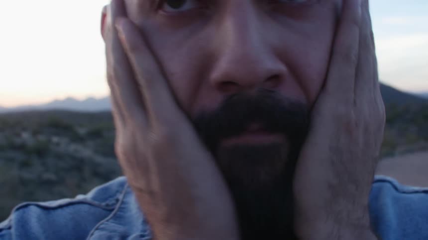 A concerned looking man rubbing his face and beard outside at sunset