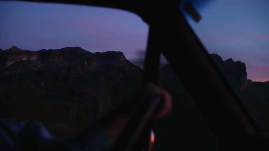 A view of a hand on a steering wheel of a vehicle driving at sunset