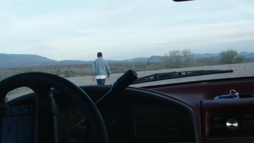 A vehicle with a steering wheel and windshield with a man walking a mountain range the sky and clouds in the background