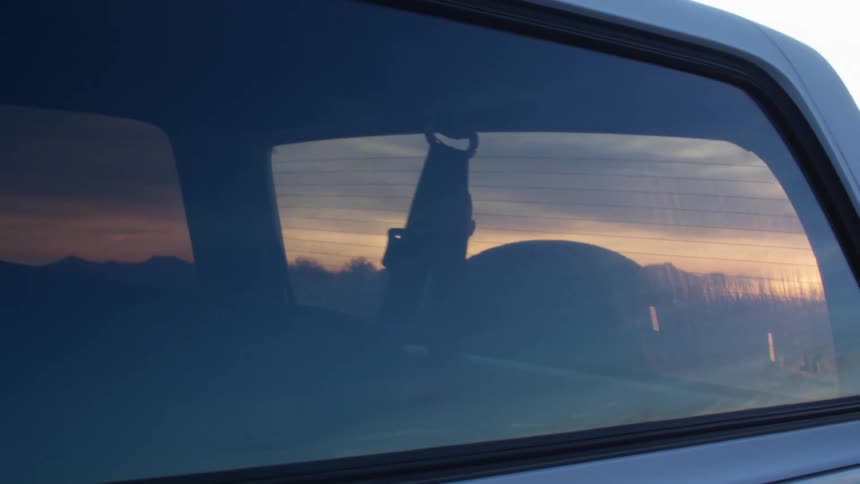 Man looking at the sunset on a rural road standing behind a car