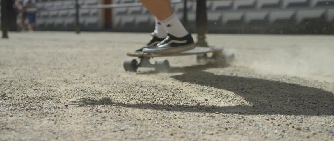 A person with sneakers and socks riding a skateboard on dirt and gravel