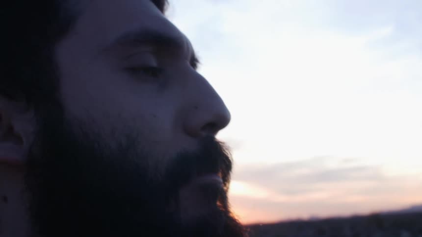 A man spits and smokes a cigarette while standing in the desert at sunset