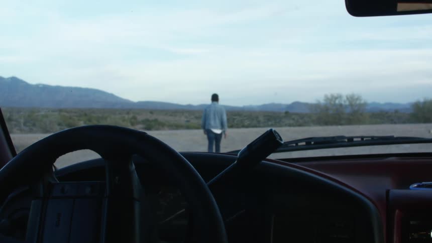 A man walks through the countryside away from a parked vehicle during the day