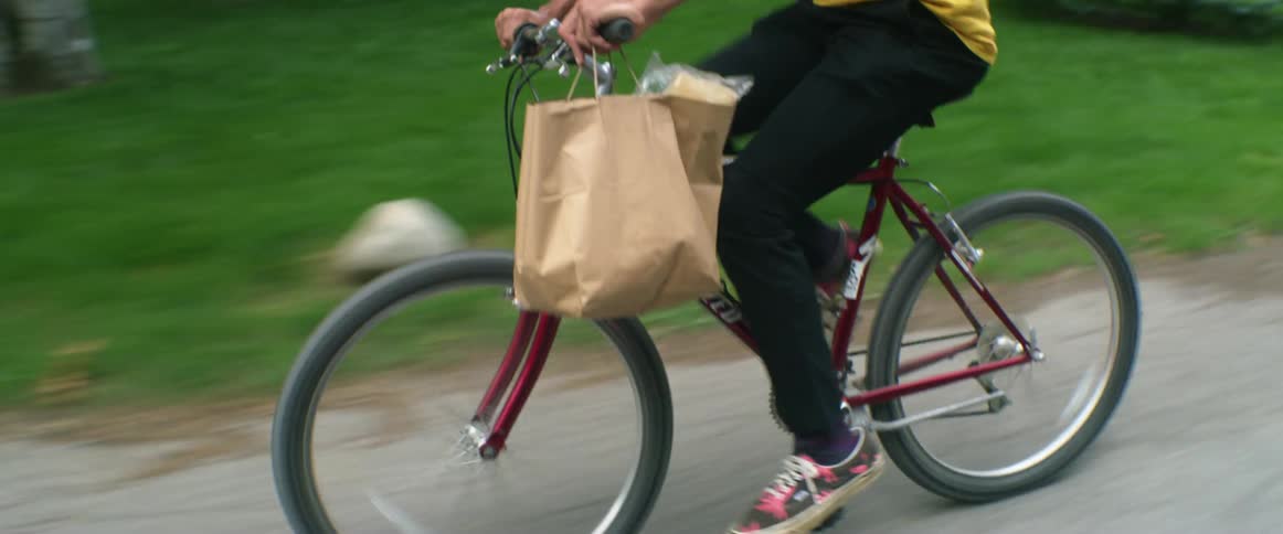 A delivery driver rides a bicycle around a curve in a neighborhood with manicured lawns