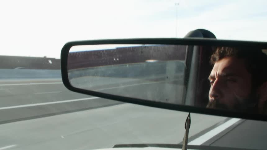 A man reflected in a rearview mirror while driving a car in the daytime
