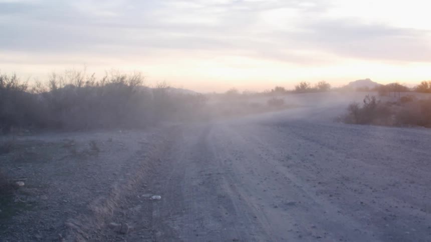 Heavy dust forms a haze over a long dirt road