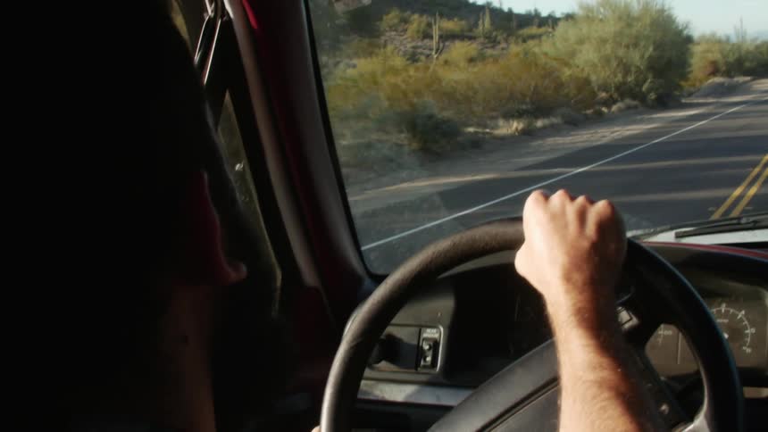 A man drives a vehicle along a road through an arid countryside during the day