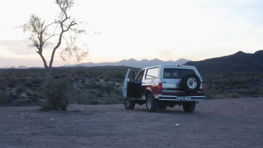 Bearded man boarding a pickup truck parked on a rural area near the desert
