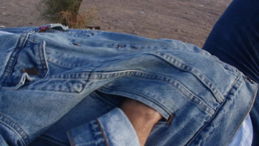 A yougng man laying on the ground puts his hand inside the pocket of a denim jacket